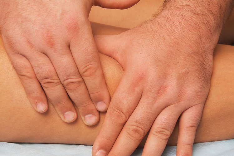 Zwei männliche Hände massieren ein Bein