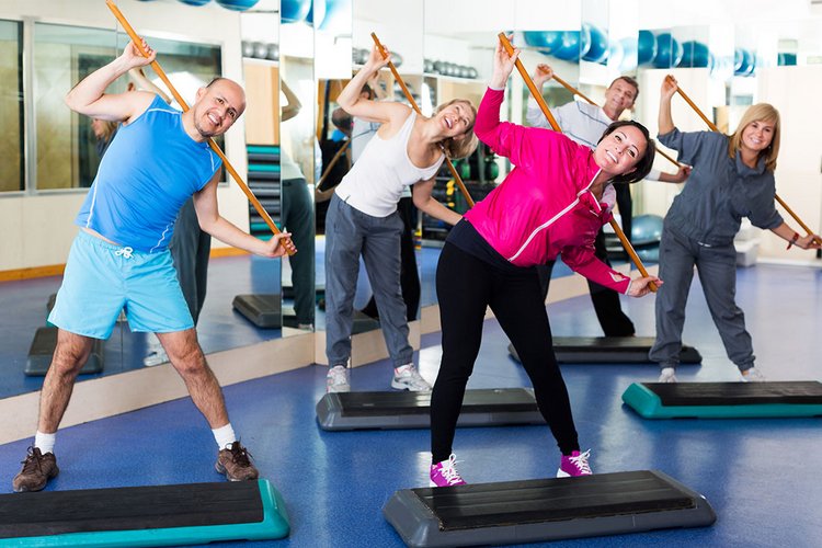 Eine Gruppe mehrerer Menschen steht in einem Sportraum und macht eine Fitnessübung