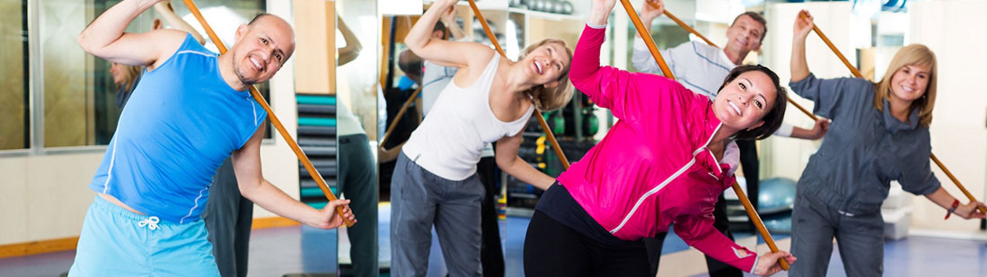 Eine Gruppe mehrerer Menschen steht in einem Sportraum und macht eine Fitnessübung