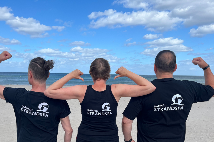 Drei Personen stehen am Strand mit dem Rücken zur Kamera