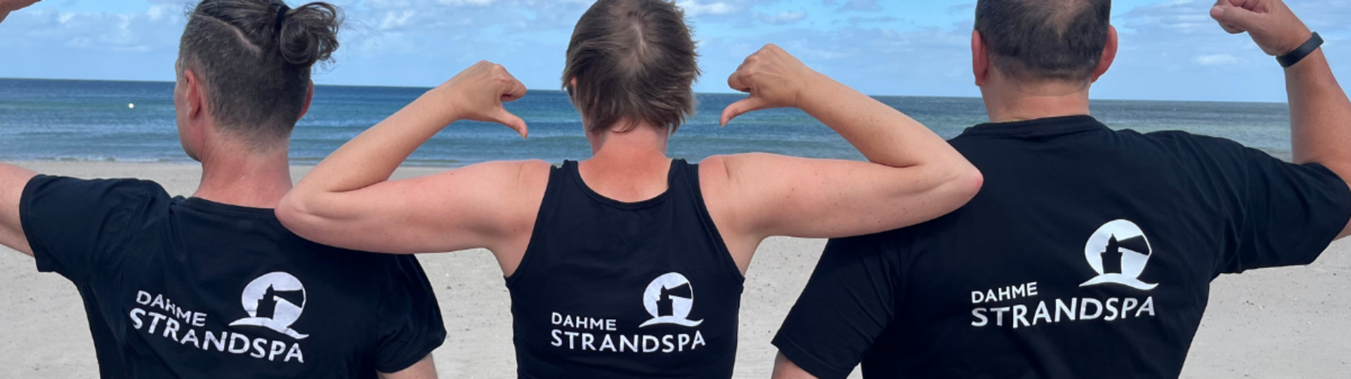 Drei Personen stehen am Strand mit dem Rücken zur Kamera