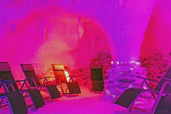 Leere Liegestühle stehen in einer pink angeleuchteten Grotte