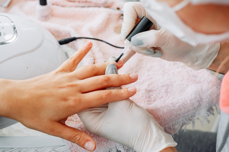 Behandschuhte Hände tragen bei einer anderen Hand Nagellack auf