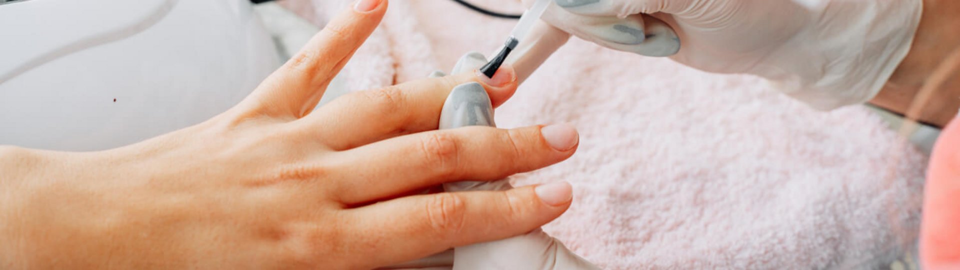Behandschuhte Hände tragen bei einer anderen Hand Nagellack auf