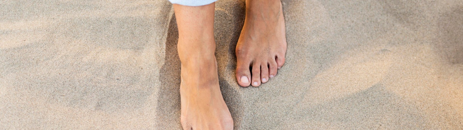Zwei nackte Füße stehen im Strandsand