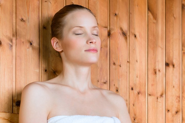 Eine Frau sitzt mit geschlossenen Augen in einer Sauna