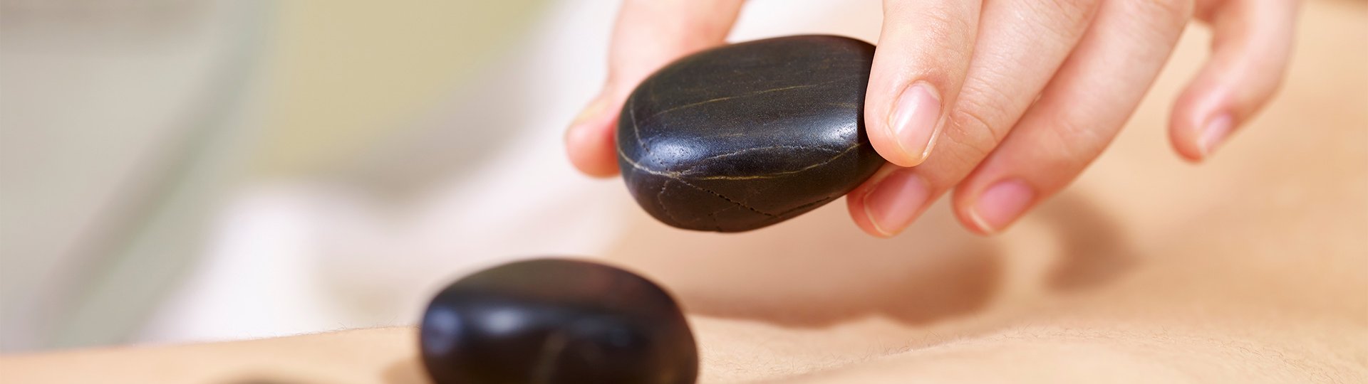 Ein weibliche Hand legt schwarze Steine auf einen Rücken