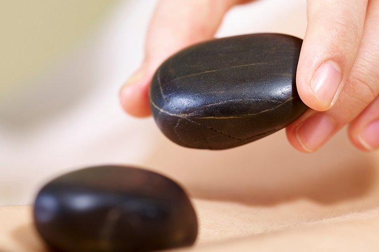 Ein weibliche Hand legt schwarze Steine auf einen Rücken