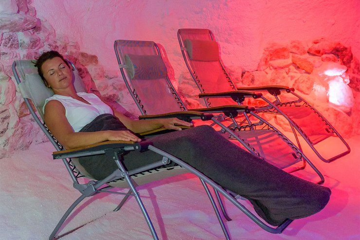 Eine Frau liegt mit geschlossenen Augen im Liegestuhl, der sich in einer pink ausgeleuchteten Grotte steht