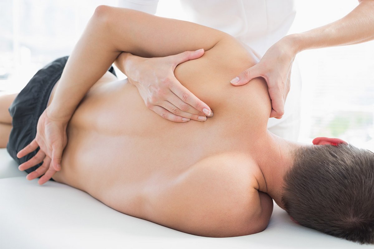 Eine Physiotherapeutin presst ihre Finger unter das Schulterblatt eines jungen Mannes