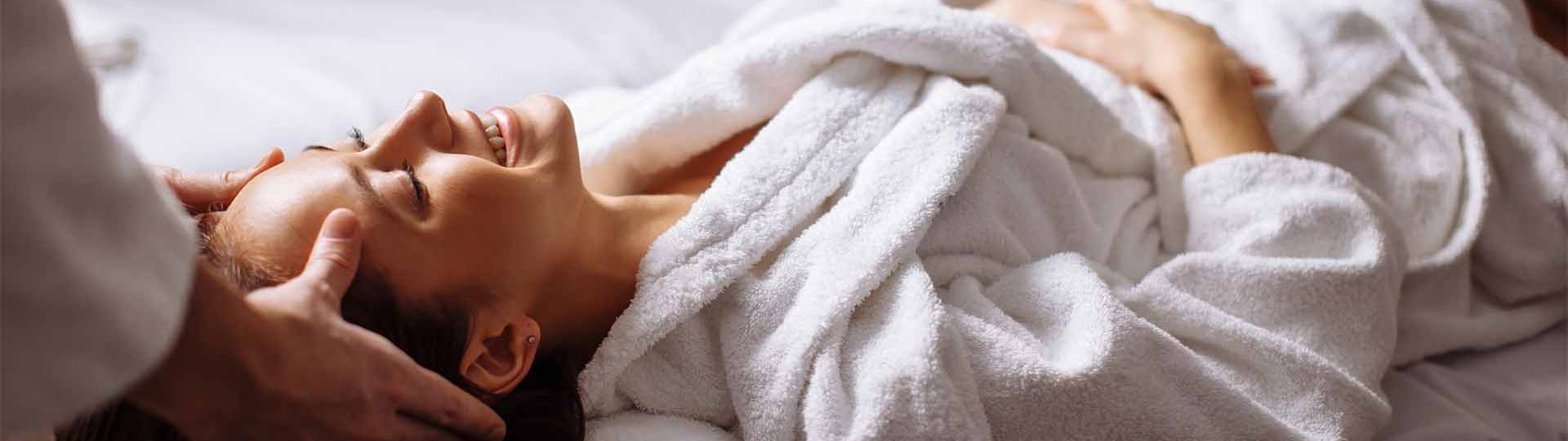 Eine lächelnde Frau im Bademantel wird am Kopf massiert