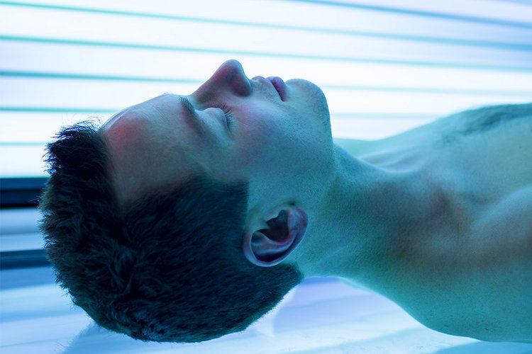 Ein junger Mann liegt in einem blau beleuchteten Solarium